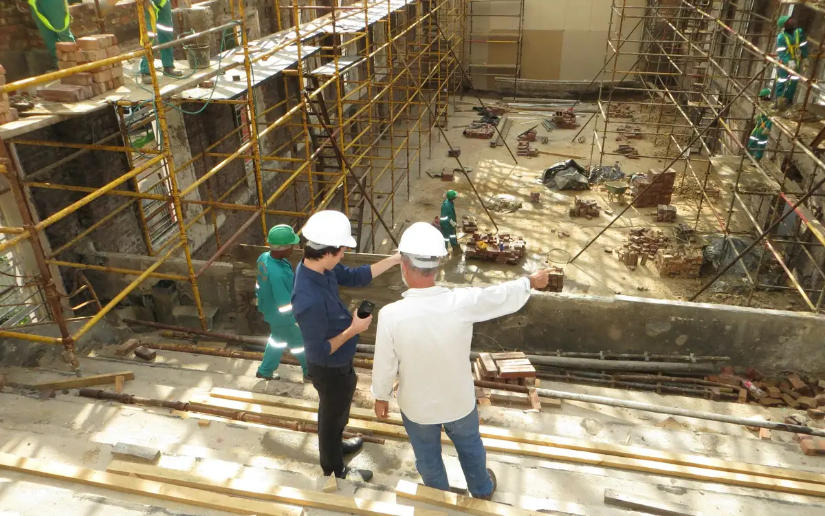 Dos responsables de obra señalan los trabajos pendientes desde lo alto de una obra con andamios