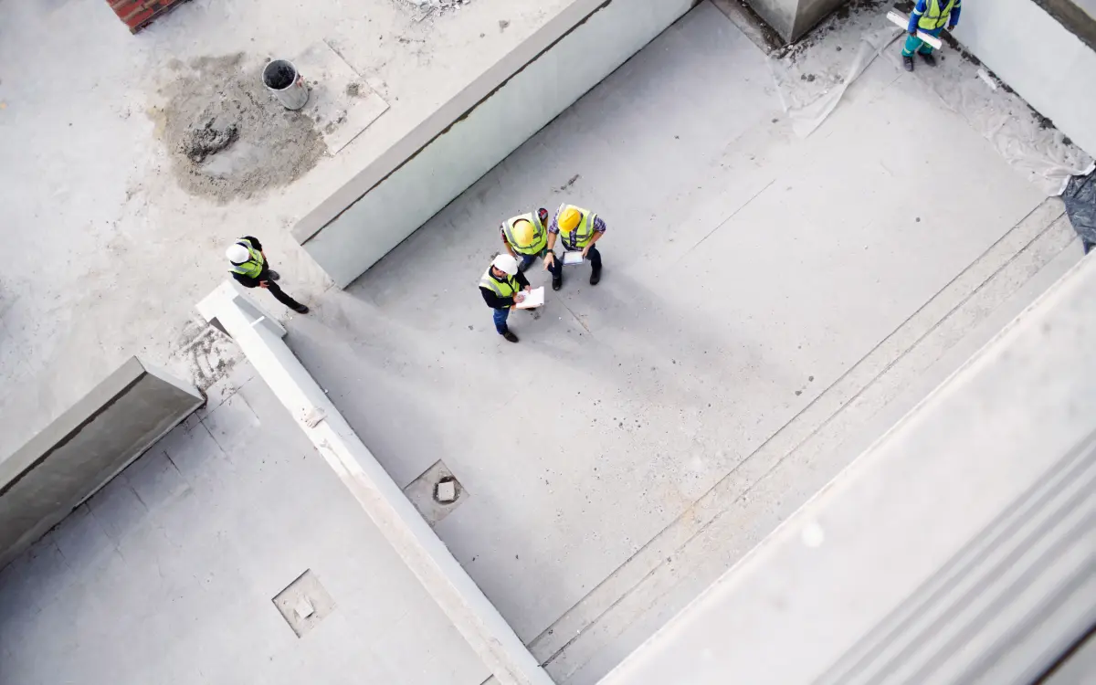 Tres responsables de obra reunidos sobre un documento en la planta de una construcción, revisando un cambio antes de aprobarlo