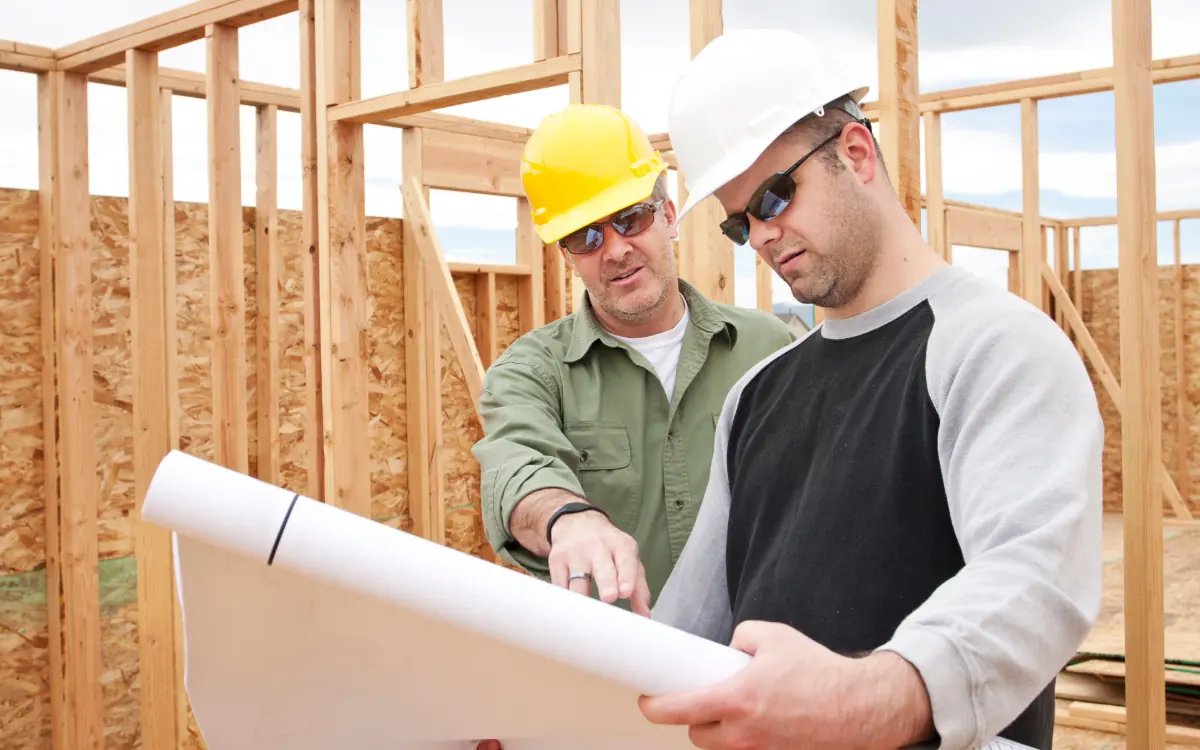 Jefe de obra revisando los planos con un trabajador dentro de una estructura en construcción