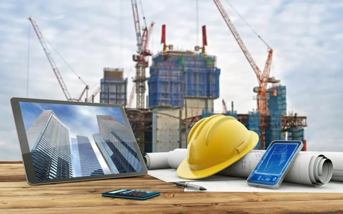 Tablet, celular y casco de obra sobre planos, con una construcción de fondo, representando las herramientas digitales de gestión de obra