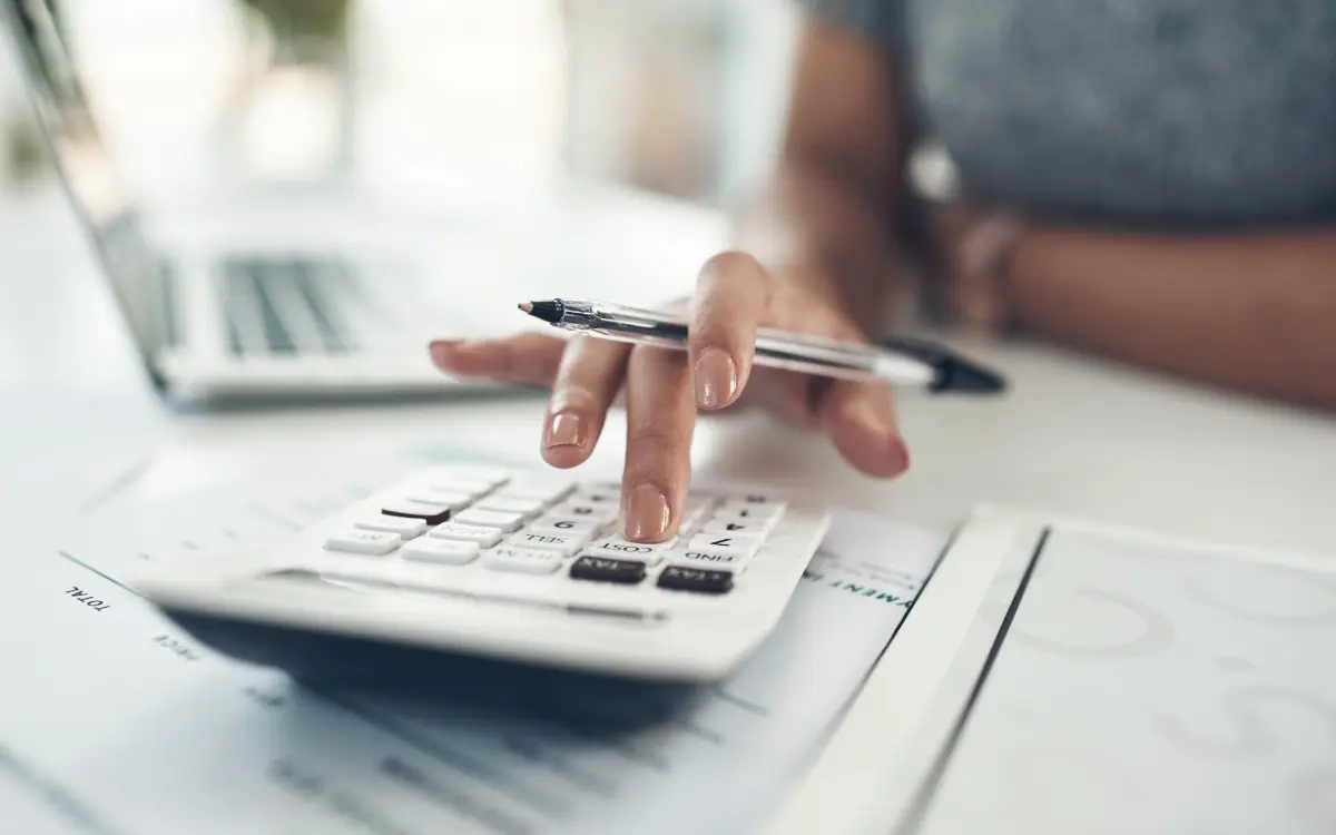 Persona calculando el presupuesto de una obra con calculadora, bolígrafo y documentos sobre la mesa