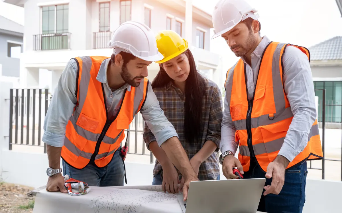 Equipo de obra revisando el programa de trabajo en una laptop y los planos frente a la construcción
