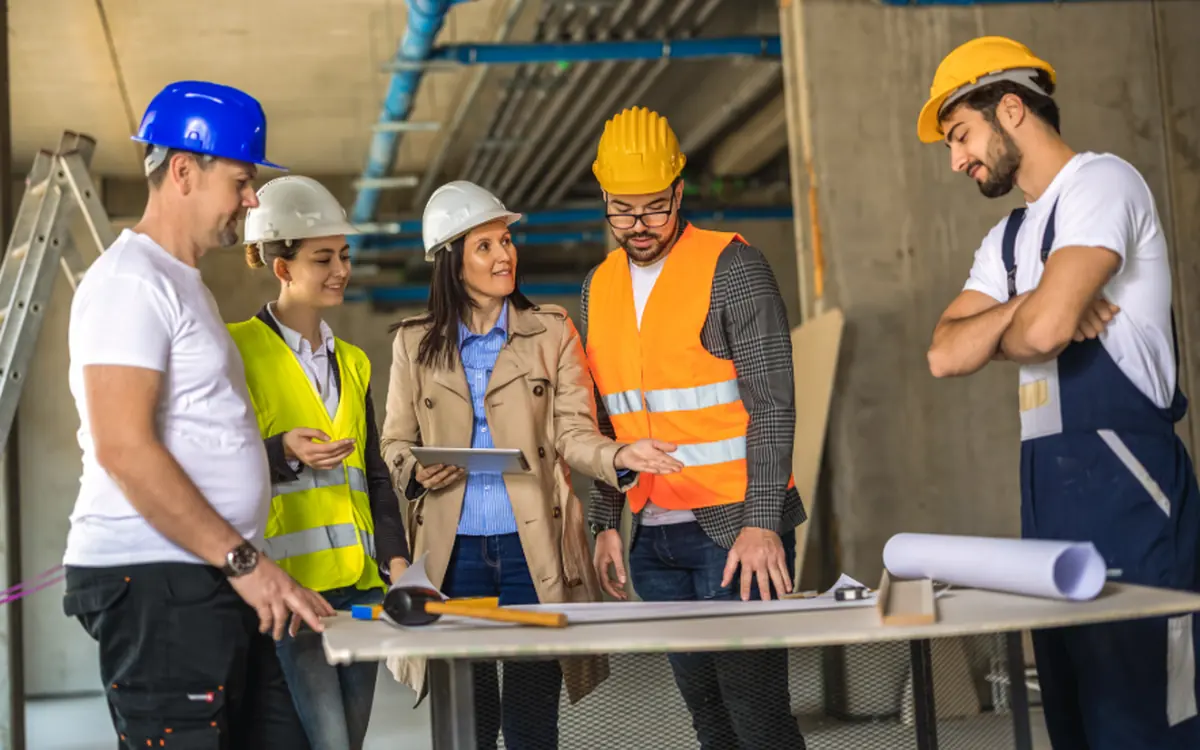 Crew in hard hats and protective equipment reviewing drawings on a table on site